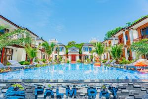 a large swimming pool with palm trees and buildings at Palm Bay Resort Phu Quoc in Phú Quốc