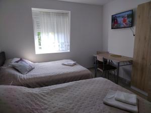 a bedroom with two beds and a desk and a window at Studio apartman MIR in Kanjiža