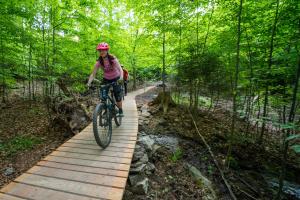 a woman riding a bike on a wooden trail at J-H APARTMÁNY HORSKÝ RESORT BUKOVÁ HORA - 100 m od LANOVKY in Červená Voda