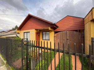 Casa amarilla con techo rojo y valla de madera en Alojamiento Sandra - Habitación 02 en Villarrica