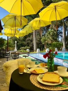 uma mesa com comida para o pequeno-almoço e guarda-sóis amarelos ao lado de uma piscina em Pousada Serra das Araucárias em São Roque