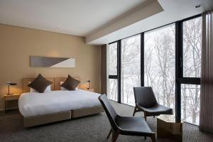 a bedroom with a bed and a chair and windows at Kozue in Niseko