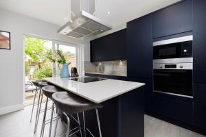 a kitchen with blue cabinets and a counter with stools at The Farnborough Wonder - Stunning 4BDR House with Garden in Farnborough