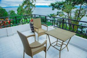 balcón con 3 sillas, mesa y vistas al agua en KIGUFI HILL, Agape Resort & Kivu Edge, en Gisenyi