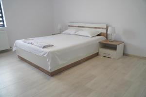 ein weißes Schlafzimmer mit einem Bett und einem Nachttisch in der Unterkunft Vila Exclusive in Târgu Jiu