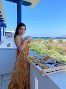 una mujer parada en un balcón con una bandeja de comida en Alykes Studios & Suites, en Agios Prokopios