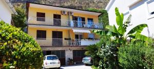 a yellow building with balconies and cars parked on the street at Guesthouse Gavrilović 28 A in Njivice
