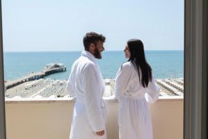 mężczyzna i kobieta stojący na balkonie z widokiem na ocean w obiekcie Grand Hotel & Riviera w mieście Lido di Camaiore
