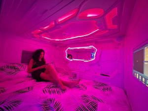 una mujer sentada en una cama en una habitación rosa en GOOD VIBES ONLY Capsule Hostel Malaga, en Málaga