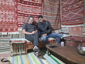 two men sitting on a bench in a room with rug at Dar Fatma Toujane in Tūjān