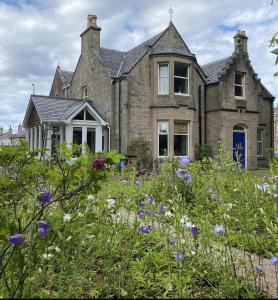 an old stone house with flowers in front of it at Glen Lyon Lodge Bed and Breakfast in Nairn