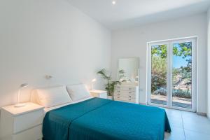 a white bedroom with a blue bed and a window at Villa Sortis in Pag