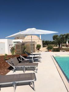 een rij ligstoelen en een parasol naast een zwembad bij Trullo Masso Antico in Alberobello