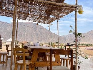 a wooden table and chairs under a straw umbrella at Cozy farm studio in Nuweiba