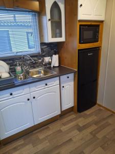 a kitchen with white cabinets and a sink and a microwave at Millfields 4 berth caravan DG & CH family's only and lead person must be over 30 in Ingoldmells