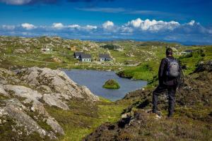 a man with a backpack standing on a hill overlooking a lake at Arran Lodge, Isle of Harris in Manish