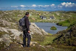 un hombre con una mochila de pie en una montaña mirando un lago en Arran Lodge, Isle of Harris, en Manish