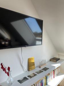 a television on a wall above a shelf with books at Le Verger de Sophie in Sainte-Geneviève-lès-Gasny