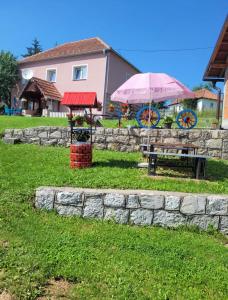 a stone wall with a table and a pink umbrella at Odmorište Vrelo Vape in Sjenica