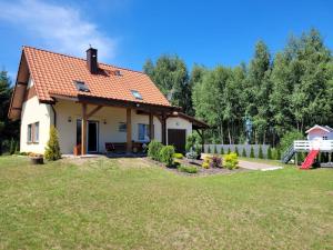 a small white house with an orange roof at Villa Grunwald - dom z działką 3000m2 na wyłączność, z dużym ogrodem, tarasem, grillem, hamakami, domkiem dla dzieci i boiskiem in Gierzwałd