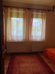 a bedroom with two windows with pink curtains and a rug at Somogyfajsz in Somogyfajsz