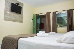 a bedroom with two beds and a tv on the wall at Pousada Aeroporto in Parnaíba