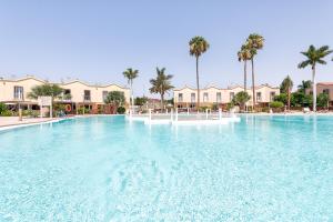 a large swimming pool with palm trees and houses at Sweet Holidays in Maspalomas