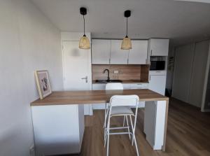 une cuisine avec des placards blancs et un comptoir avec deux tabourets dans l'établissement Appartement proche plages, à Brancieux