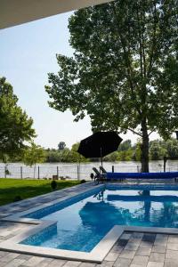 a swimming pool with an umbrella next to a lake at Drinska Prica - Vikendica na Drini in Loznica