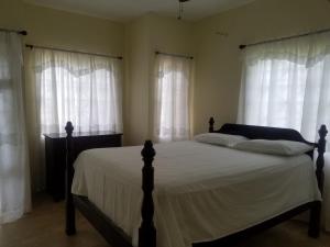 a bedroom with a bed with white sheets and windows at Rio View Apartments in Ocho Rios