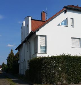 une maison blanche avec une haie devant elle dans l'établissement Berlin-Oase - schnuckelige Ferienwohnung an der Grenze zu Berlin, à Schönefeld