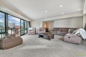 a large living room with a couch and chairs and windows at QV Stays Front Stage City Lights in Auckland