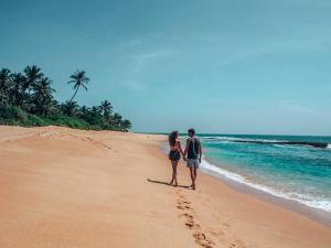 a man and a woman walking on the beach at NALENDRA ROOMS - Oceanfront in Boossa +8 photos