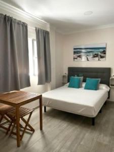 Schlafzimmer mit einem Bett mit blauen Kissen und einem Tisch in der Unterkunft Habitaciones Turísticas - La Tarayuela in Barbate