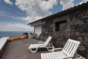 2 sillas blancas sentadas en el patio de una casa de piedra en Casas da Pedreira, en Lajes do Pico