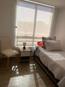 a bedroom with a bed and a chair and a window at Departamento con piscina. in Viña del Mar