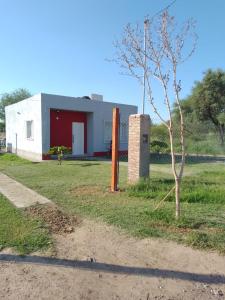 um edifício branco com uma porta vermelha e uma árvore em casa pileta patio indio froilan estadio unico madre de ciudades em Santiago del Estero