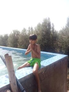 a young boy sitting on the edge of a swimming pool at Nuit dans la ferme in Marrakech