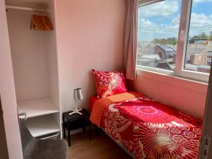 a small bedroom with a red bed and a window at Glücklich am Meer Meerblick mit Wellnesszugang in Egmond aan Zee