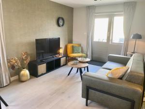 ein Wohnzimmer mit einem Sofa und einem Flachbild-TV in der Unterkunft Glücklich am Meer Meerblick mit Wellnesszugang in Egmond aan Zee