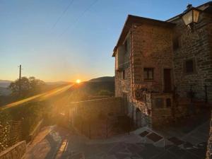 um antigo edifício de pedra com o pôr-do-sol ao fundo em Iris Country House em Ortignano Raggiolo
