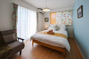 a bedroom with a bed with a chair and a window at 海まで徒歩1分・浜比嘉島まで車で10分！12名宿泊可能な和室ありの宿泊施設 ホームプラスアール in Uruma
