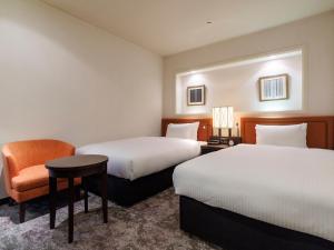 um quarto de hotel com duas camas e uma cadeira em JR Kyushu Hotel Blossom Fukuoka em Fukuoka