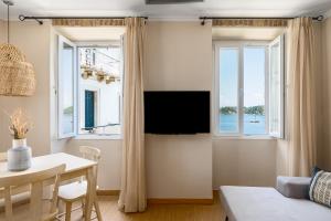a living room with a table and a tv and two windows at Fotiadis Family Luxury Suites by Konnect in Corfu Town
