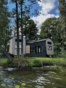 a black tiny house sitting next to a river at Tiny House - Osada Wilkasy in Giżycko