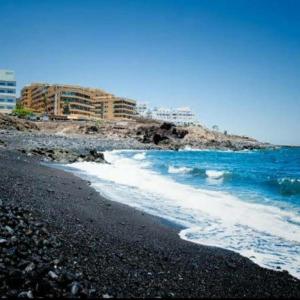 a beach with a black sand and blue water and buildings at 349 Apartamento Golf del Sur Albatros in San Miguel de Abona