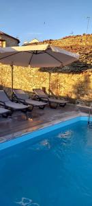 a pool with chairs and umbrellas next to a stone wall at A Casa Alegre in Miranda do Douro