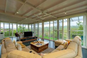 sala de estar con sofás, TV y ventanas en The Glasscape by StayVista - Hillside getaway with Pool and Indoor games, en Nashik