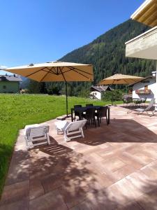 een patio met een tafel, stoelen en parasols bij Appartamento Mary - Casa Green - Dog friendly, box auto in Cogolo