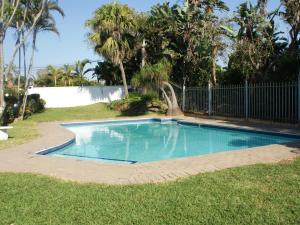 a swimming pool in a yard with a fence and palm trees at Mangrove Beach Estate - 3 Mtwalume in Port Shepstone